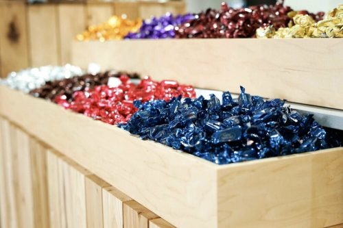 Colorful assorted candies in shiny wrappers displayed in wooden bins.