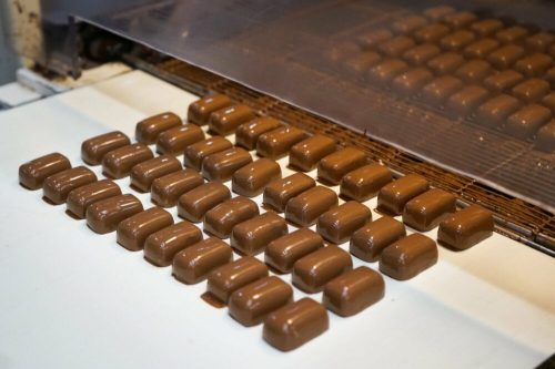 Rows of freshly molded chocolate candies on a conveyor belt in a factory setting.