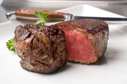 A perfectly cooked steak on a white plate, showcasing a seared exterior and juicy pink interior.