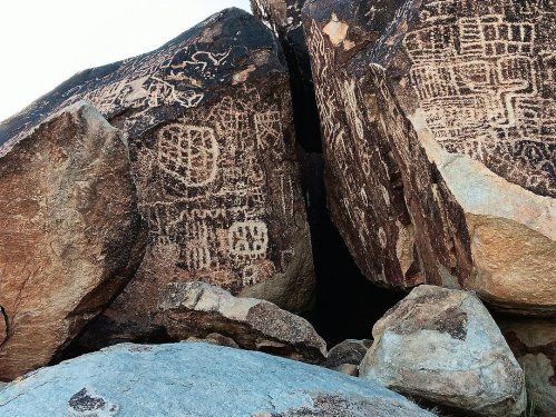 Petroglyphs carved into large boulders, showcasing intricate designs and patterns in a natural rocky setting.