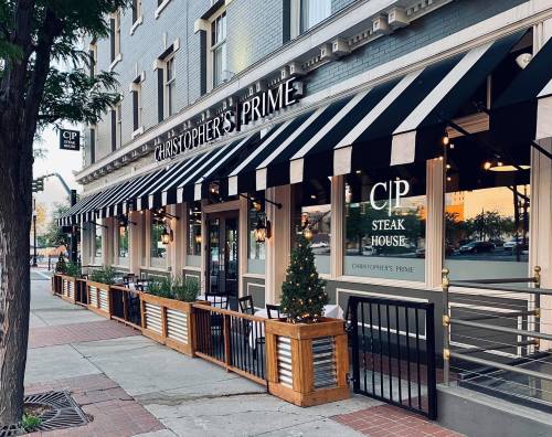 Exterior of Christopher's Prime Steak House, featuring striped awnings, outdoor seating, and festive decor.