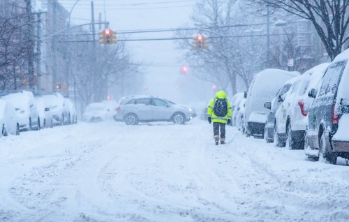 City streets during a snowstorm, with heavy snowfall and cars covered in snow.