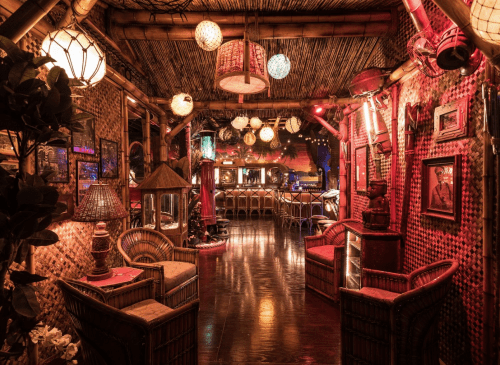 A cozy tiki bar with bamboo decor, colorful lanterns, and warm lighting, featuring wicker seating and a vibrant atmosphere.