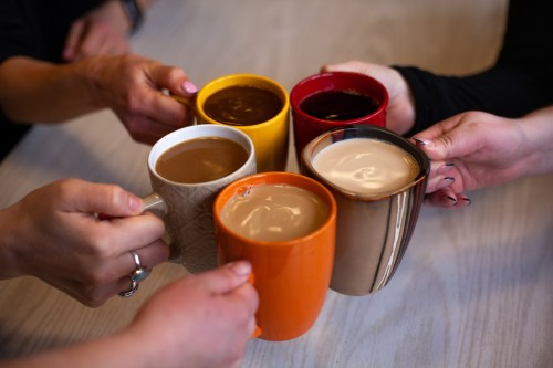 Five hands holding colorful mugs of coffee, clinking together in a cheerful toast.