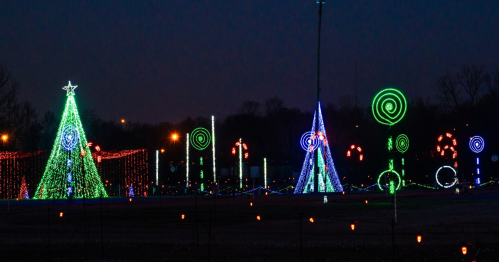 Colorful holiday lights illuminate trees and decorations in a park at dusk, creating a festive atmosphere.