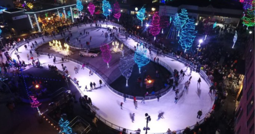 Aerial view of a bustling ice skating rink surrounded by colorful lights and a festive crowd.
