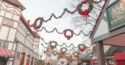 Festive decorations with wreaths and bows adorn a charming street lined with traditional buildings.