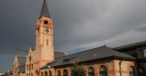 Historic building with a tall clock tower, featuring stone and brick architecture under a cloudy sky.