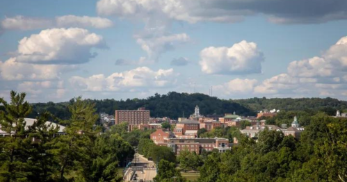 A scenic view of a town with buildings and trees, set against a backdrop of blue sky and fluffy clouds.