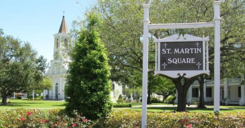 Sign for St. Martin Square with a church in the background, surrounded by trees and colorful flowers.