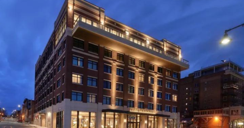 A modern brick building illuminated at dusk, featuring large windows and a welcoming entrance.