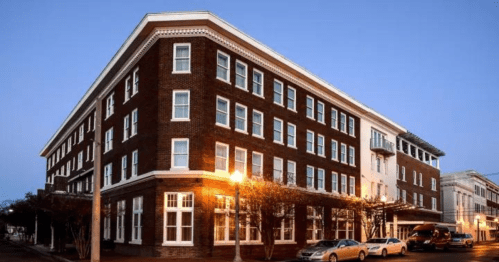 Historic brick building with large windows, featuring a corner entrance and streetlights, at dusk.