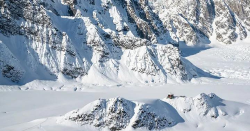 A snowy mountain landscape with steep cliffs and a small building nestled among the snow-covered peaks.