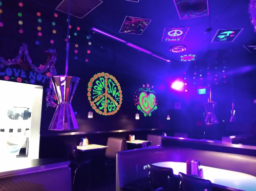 A vibrant diner interior with colorful neon decorations, glowing artwork, and retro-style seating under purple lighting.