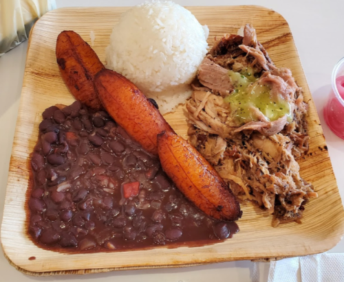 A plate of rice, black beans, fried plantains, and shredded meat with green sauce.