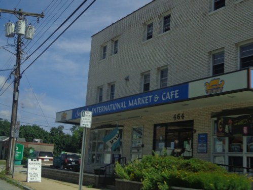 Exterior of a building featuring "International Market & Café" sign, with a parking area and power lines in the background.