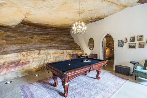 A unique game room with a pool table, chandelier, and natural rock walls, featuring a cozy, rustic atmosphere.