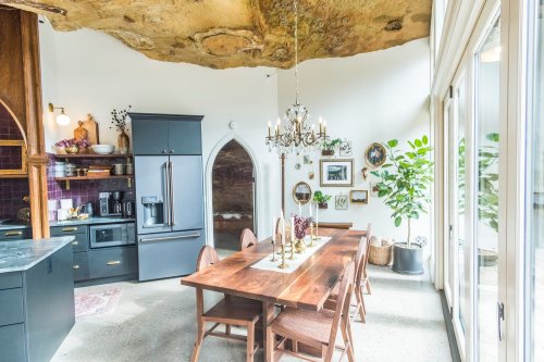 A modern kitchen with a wooden dining table, elegant chandelier, and a unique rock ceiling feature.