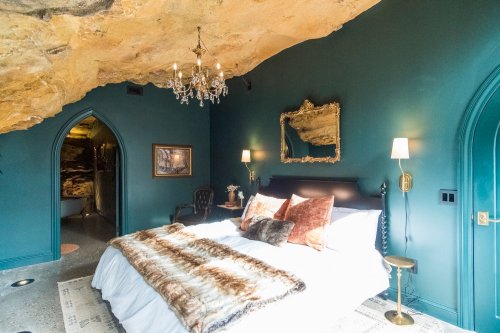 Cozy bedroom with a rock ceiling, dark green walls, elegant chandelier, and plush bedding.