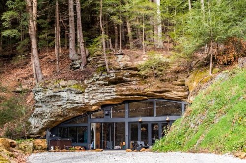 A modern home built into a rocky hillside, surrounded by tall trees and natural landscape.
