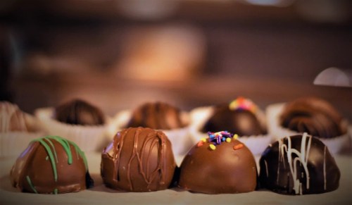 A close-up of assorted chocolate truffles, some decorated with colorful sprinkles and drizzles.
