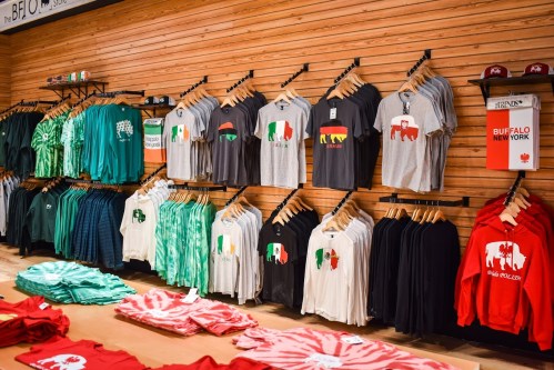 A display of various t-shirts in a store, featuring different colors and designs, hanging on wooden racks.