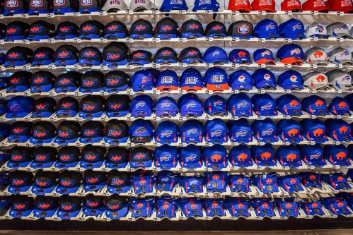 A display of various blue and red hats featuring sports team logos, neatly arranged on shelves.