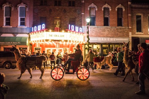A festive street scene with people and llamas parading in front of a vintage theater, illuminated at night.