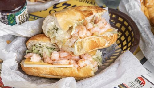 A close-up of a shrimp sandwich with lettuce and cheese, served in a basket with a drink in the background.