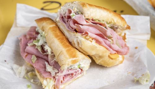 A close-up of a sandwich filled with layers of ham, lettuce, and cheese, served on a toasted hoagie roll.