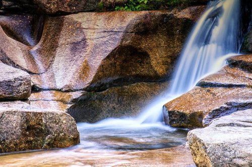 A serene waterfall cascading over smooth rocks, surrounded by lush greenery and a tranquil pool below.
