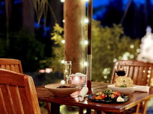A cozy outdoor dining setup with a candle, wine, and two plates of food, surrounded by soft lights at dusk.