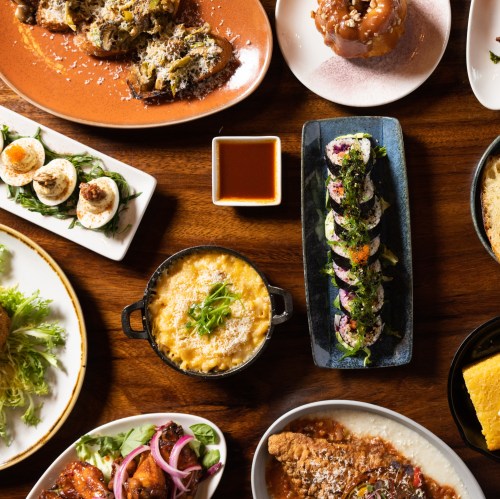 A variety of dishes including sushi, dumplings, and salads arranged on a wooden table.