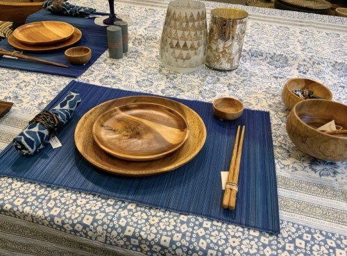 A beautifully set table with wooden dishes, chopsticks, and decorative bowls on a patterned blue tablecloth.