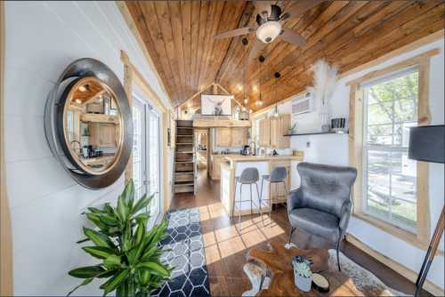 Cozy interior of a tiny house featuring wooden beams, a kitchen, a living area, and a decorative plant.