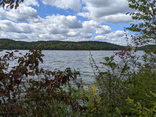 A serene lake surrounded by lush greenery and hills under a partly cloudy sky.