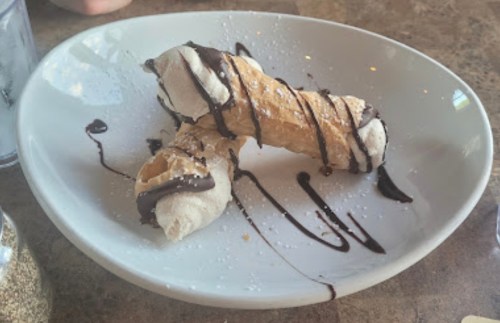 Two cannoli on a white plate, drizzled with chocolate sauce and sprinkled with powdered sugar.