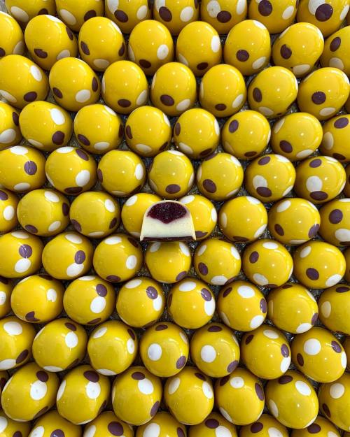 A vibrant arrangement of yellow and white spotted chocolates, with one chocolate featuring a red filling in the center.