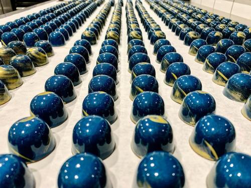 A close-up of rows of blue and gold chocolate bonbons arranged neatly on a white surface.