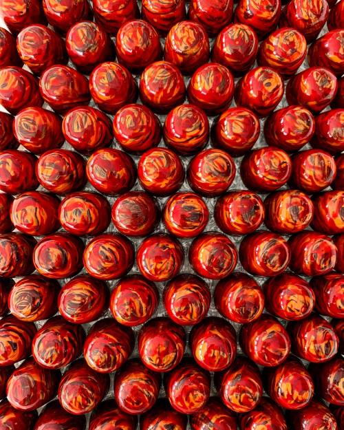 A close-up view of numerous red and orange marbled bottle caps arranged in a grid pattern.