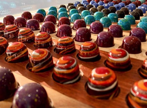A colorful array of decorative chocolate truffles arranged in rows, showcasing various vibrant designs and patterns.