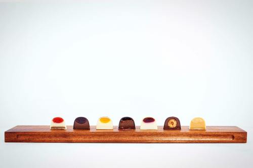 A wooden board displays an assortment of colorful chocolates, each with unique toppings and fillings.