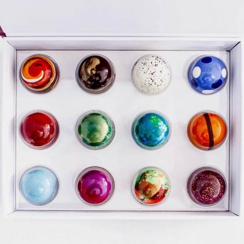 A box containing twelve colorful, spherical chocolates with various designs and patterns.