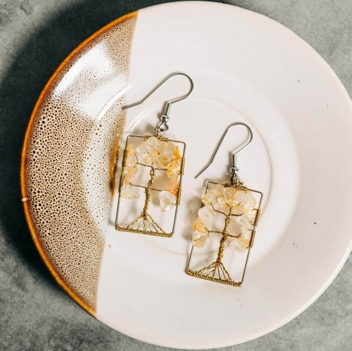 Gold wire earrings shaped like trees, adorned with clear crystal-like stones, displayed on a textured white plate.