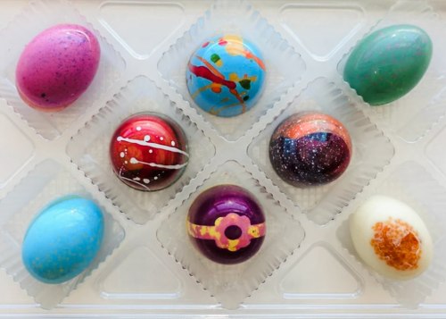 A tray of colorful, decorated Easter eggs in various patterns and shades, arranged in a clear plastic container.