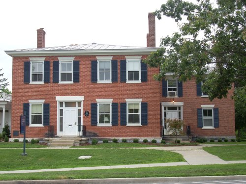 A two-story brick house with blue shutters, a white door, and a manicured lawn.