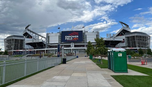 Exterior view of Empower Field, featuring a large sign and surrounding green space under a cloudy sky.