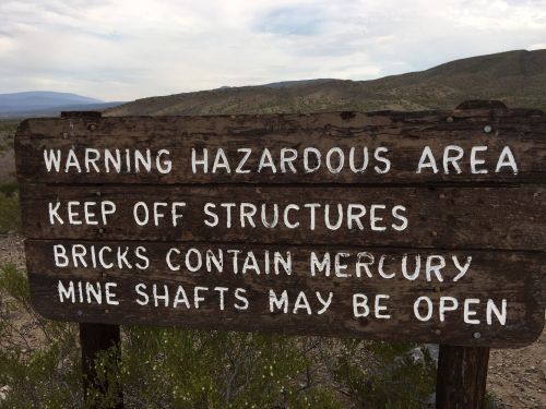 Wooden sign warning of hazardous area, advising to keep off structures due to mercury and open mine shafts.