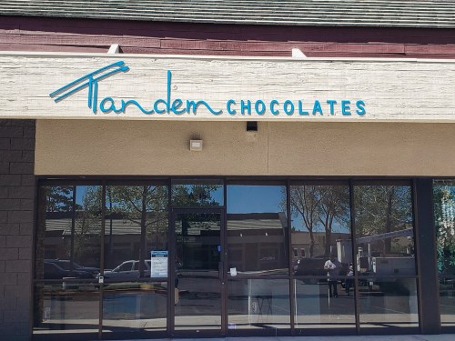 Sign for "Tandem Chocolates" on a storefront with large glass windows and a simple exterior.