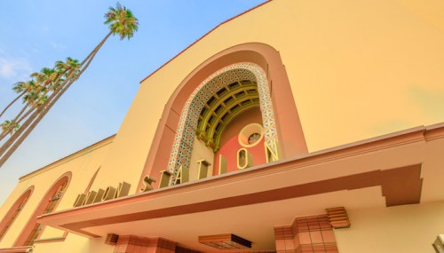 Art Deco-style building with "STATION" sign, palm trees, and a bright blue sky in the background.